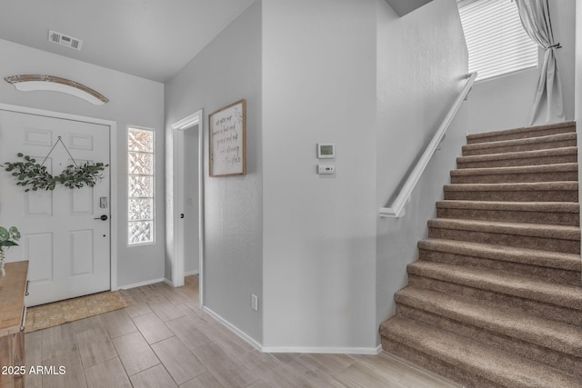 entryway featuring wood finish floors, visible vents, baseboards, and stairs