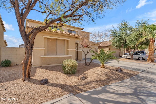 view of front of home with concrete driveway, fence, a tile roof, and stucco siding