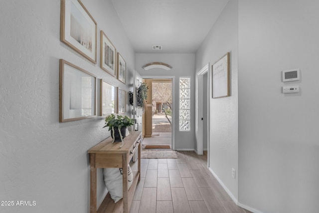 foyer entrance with baseboards, visible vents, a textured wall, and wood finish floors