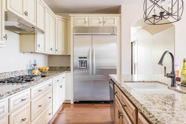 kitchen with light stone countertops, sink, stainless steel appliances, decorative light fixtures, and light wood-type flooring