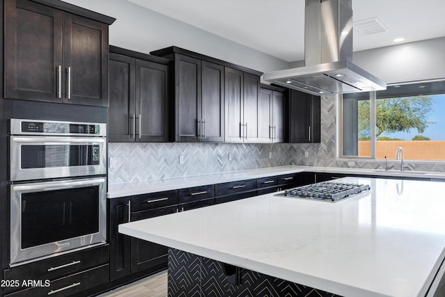 kitchen featuring backsplash, island range hood, sink, and appliances with stainless steel finishes