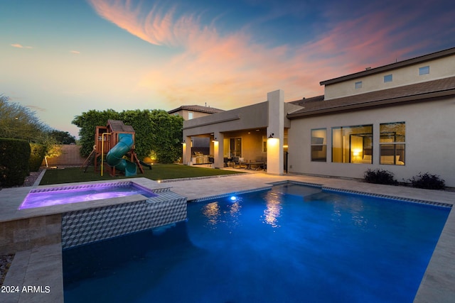 pool at dusk featuring a playground, a patio area, and an in ground hot tub