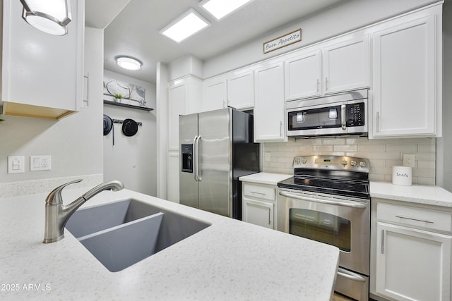 kitchen with light stone counters, a sink, stainless steel appliances, white cabinetry, and backsplash