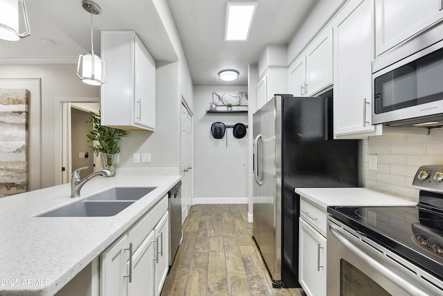 kitchen featuring wood finished floors, a sink, appliances with stainless steel finishes, white cabinetry, and tasteful backsplash