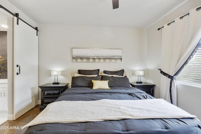 bedroom with a ceiling fan, a barn door, wood finished floors, and baseboards