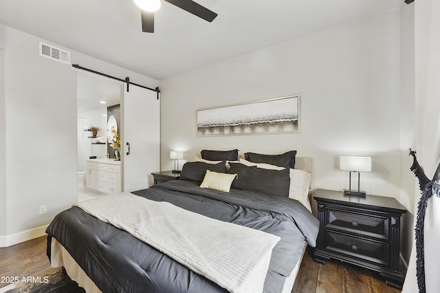 bedroom featuring wood finished floors, visible vents, baseboards, ensuite bathroom, and a barn door