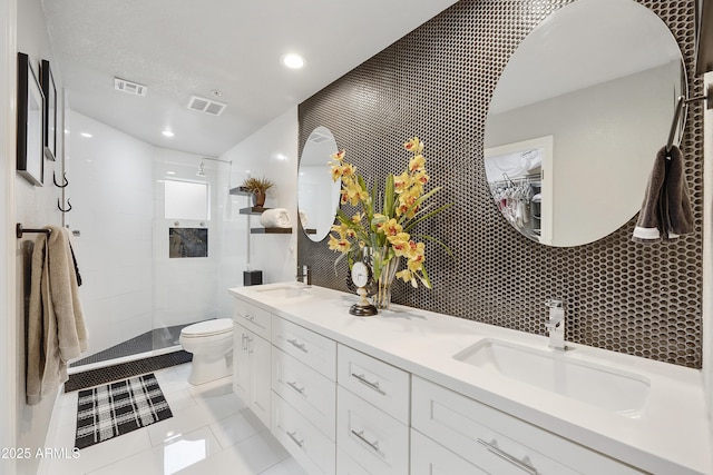 bathroom featuring a tile shower, double vanity, toilet, and a sink