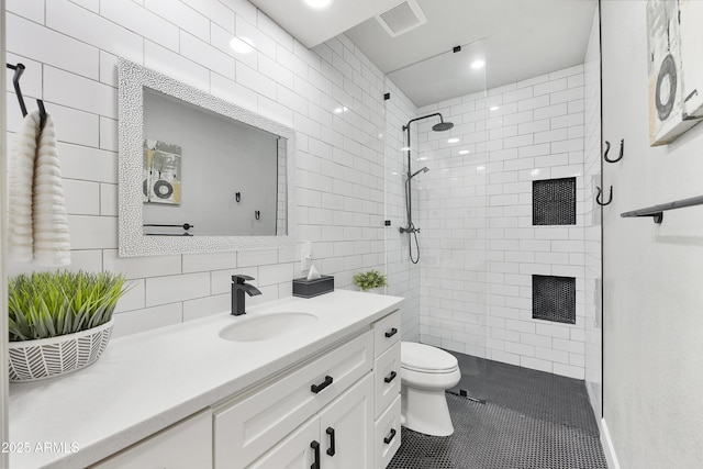 bathroom with vanity, visible vents, tiled shower, tile patterned floors, and toilet