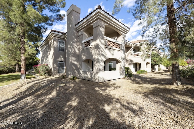 back of property with stucco siding, a tiled roof, a chimney, and a balcony