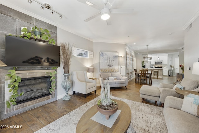 living area with visible vents, wood-type flooring, a fireplace, crown molding, and ceiling fan