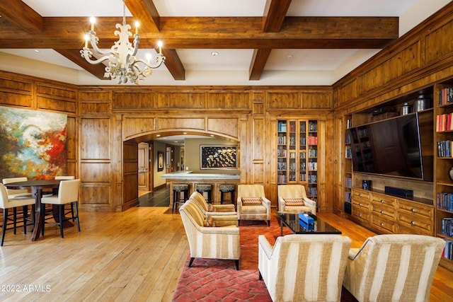 living room featuring a notable chandelier, beam ceiling, light hardwood / wood-style floors, and wood walls