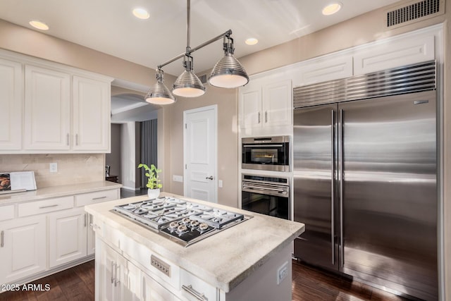 kitchen featuring appliances with stainless steel finishes, hanging light fixtures, white cabinets, a kitchen island, and dark hardwood / wood-style flooring