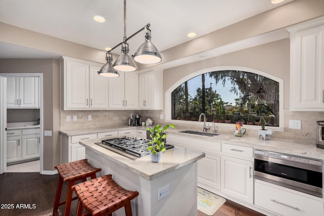 kitchen featuring sink, white cabinetry, light stone counters, stainless steel gas cooktop, and decorative light fixtures