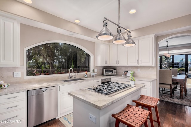 kitchen with sink, appliances with stainless steel finishes, a kitchen island, light stone countertops, and white cabinets