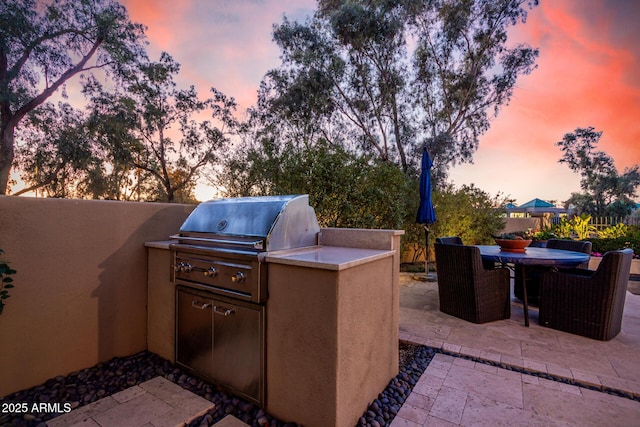 patio terrace at dusk with exterior kitchen and area for grilling