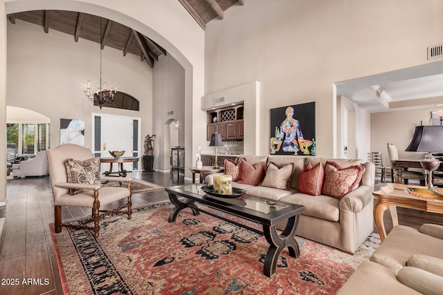 living room with a towering ceiling, hardwood / wood-style floors, a notable chandelier, and beam ceiling