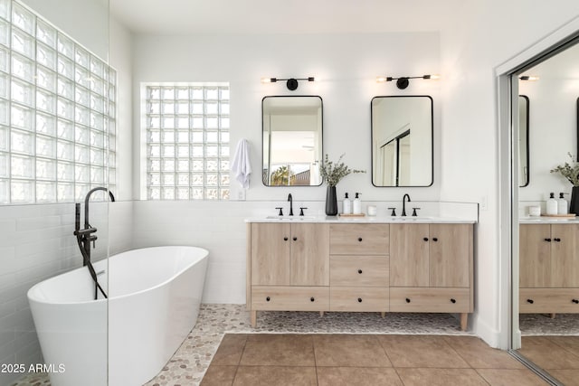 bathroom with tile patterned flooring, vanity, a washtub, and tile walls