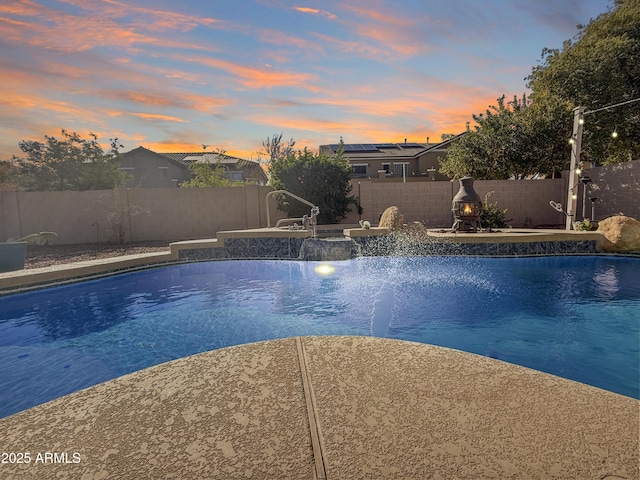 pool at dusk featuring pool water feature and a patio area