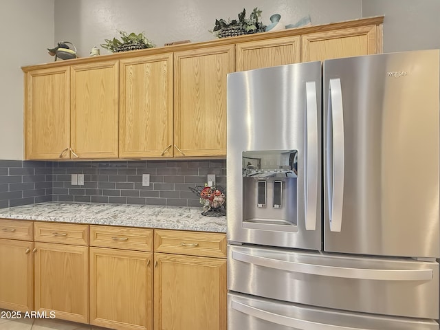 kitchen with light stone countertops, decorative backsplash, and stainless steel fridge