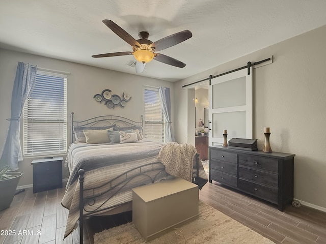 bedroom with ceiling fan, a barn door, and dark hardwood / wood-style flooring