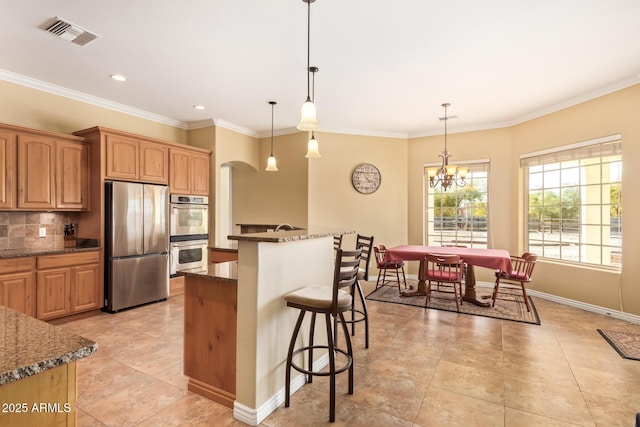 kitchen with arched walkways, visible vents, a kitchen breakfast bar, appliances with stainless steel finishes, and backsplash