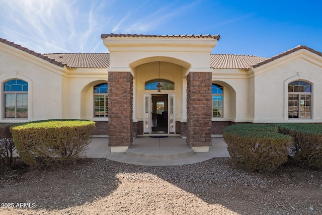 doorway to property featuring stone siding, a tile roof, and stucco siding