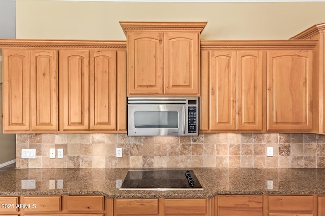 kitchen featuring tasteful backsplash, stainless steel microwave, light brown cabinets, dark stone counters, and black electric cooktop