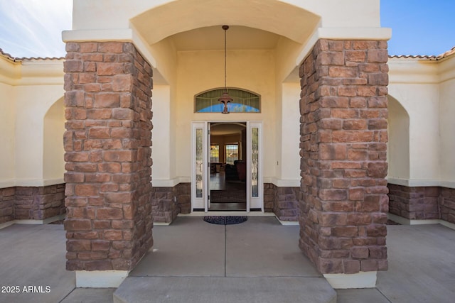 view of exterior entry featuring stone siding, a tile roof, and stucco siding