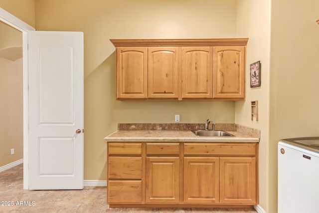 kitchen with light countertops, light brown cabinets, a sink, and baseboards