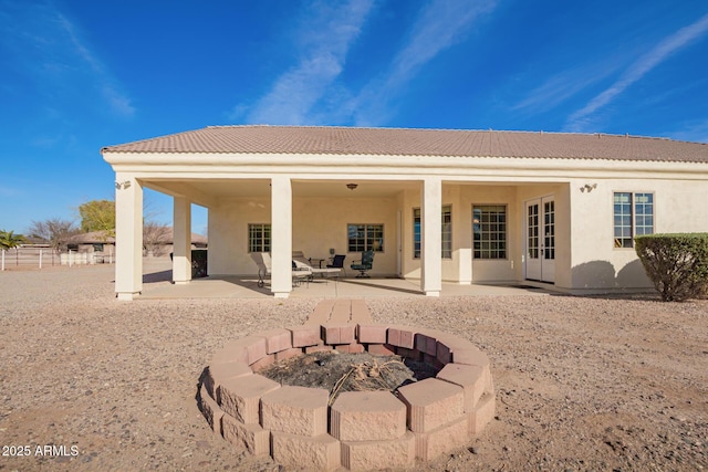 rear view of house with stucco siding, a tile roof, a fire pit, and a patio