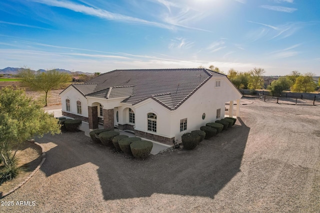 back of house with driveway, stone siding, a tile roof, and stucco siding