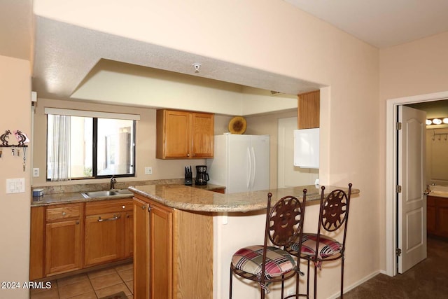 kitchen featuring sink, white fridge, a breakfast bar area, light stone countertops, and tile flooring