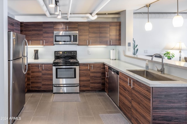 kitchen with appliances with stainless steel finishes, sink, dark tile patterned flooring, hanging light fixtures, and kitchen peninsula