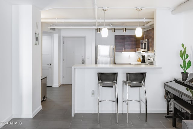 kitchen with appliances with stainless steel finishes, a kitchen bar, hanging light fixtures, kitchen peninsula, and dark brown cabinets