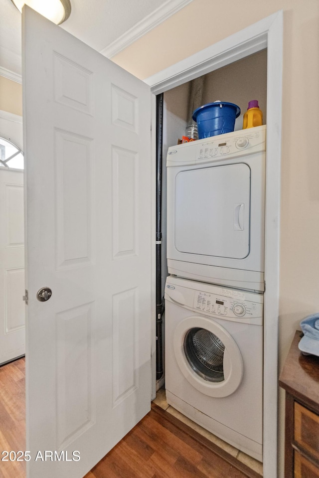 washroom featuring hardwood / wood-style flooring, ornamental molding, and stacked washing maching and dryer