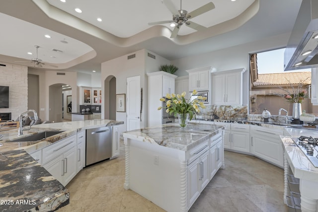 kitchen featuring a spacious island, a tray ceiling, sink, and light stone counters