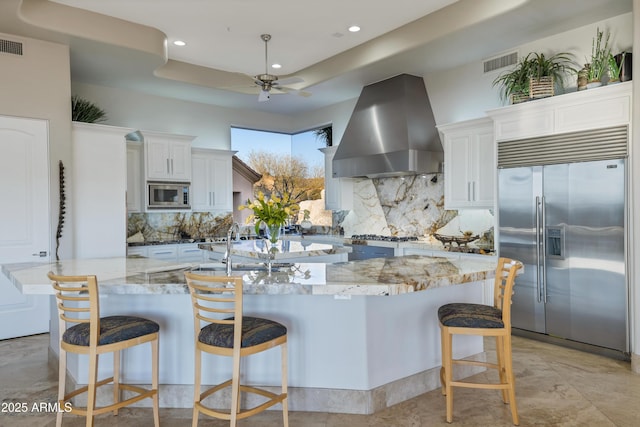 kitchen featuring a large island, built in appliances, range hood, and white cabinets