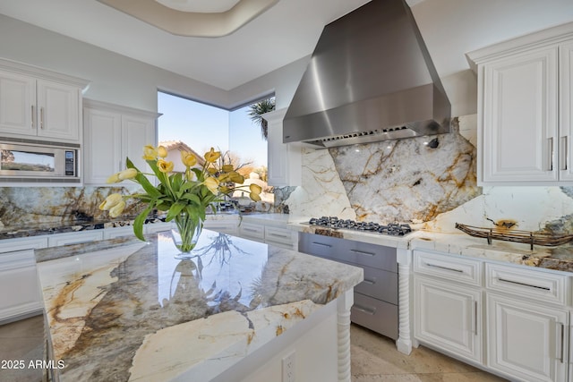 kitchen with white cabinetry, light stone counters, island range hood, and appliances with stainless steel finishes