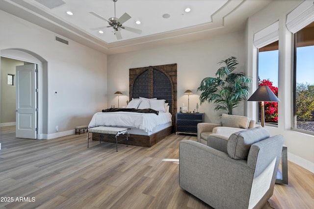 bedroom with ceiling fan, a raised ceiling, and light hardwood / wood-style floors