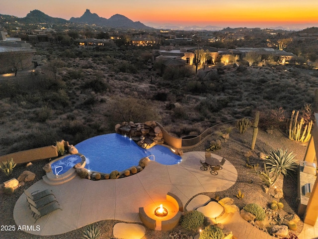 pool at dusk featuring a mountain view, a fire pit, and a patio area