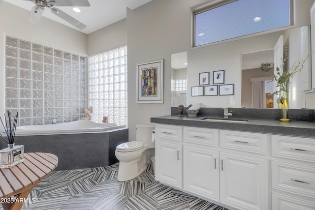 bathroom featuring toilet, vanity, ceiling fan, tiled bath, and tile patterned flooring