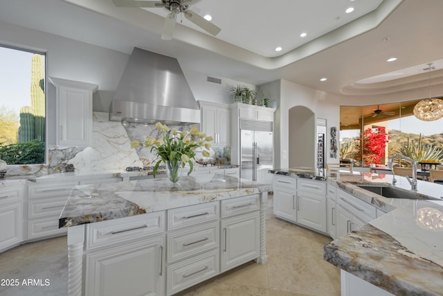 kitchen with sink, extractor fan, white cabinets, a raised ceiling, and a large island with sink