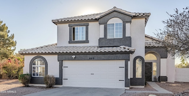 mediterranean / spanish house with driveway, a tiled roof, an attached garage, and stucco siding