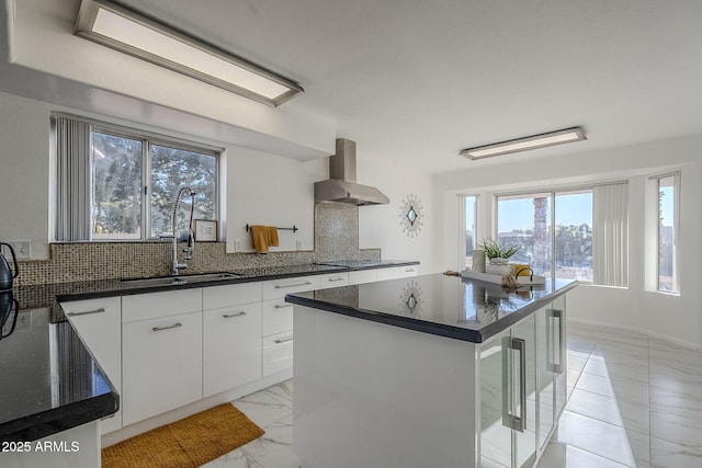 kitchen with white cabinetry, decorative backsplash, a kitchen island, wall chimney exhaust hood, and sink