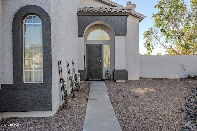 property entrance featuring fence, a tiled roof, and stucco siding