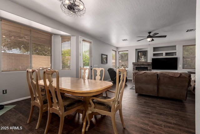 6862 W Honeysuckle Dr, Peoria, AZ 85383 - dining area featuring dark wood-type flooring, baseboards, a ceiling fan, a stone fireplace, and a textured ceiling