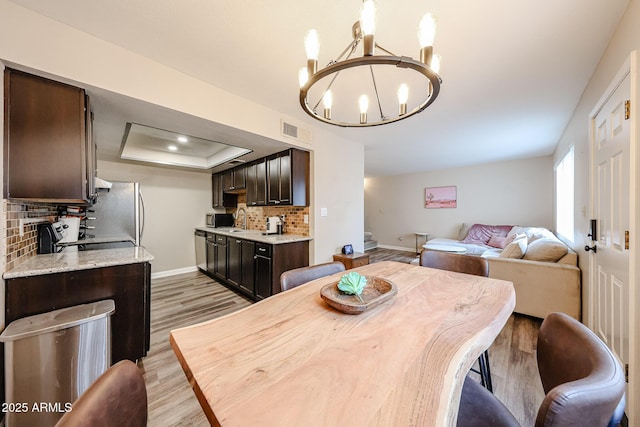 dining space with a raised ceiling, a chandelier, and light wood-type flooring