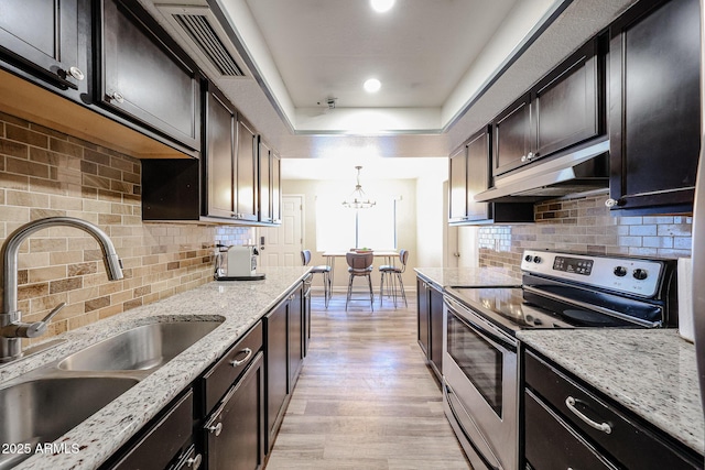 kitchen with decorative light fixtures, sink, stainless steel range with electric cooktop, a raised ceiling, and light stone countertops