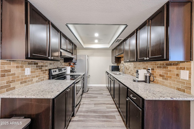 kitchen featuring a raised ceiling, light stone countertops, appliances with stainless steel finishes, and sink