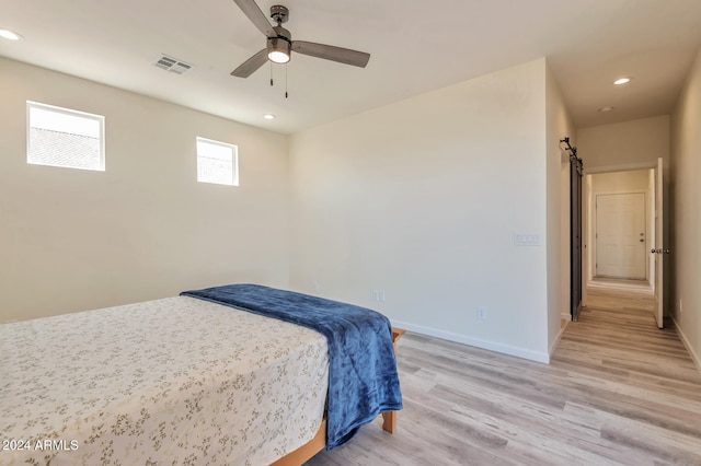 bedroom featuring a barn door, light hardwood / wood-style flooring, and ceiling fan